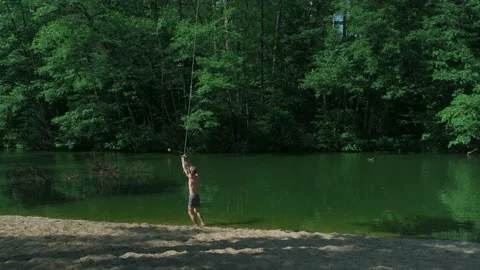The guy in the forest rides over the water bungee on a tree, jumps into the lake Stock Footage 198051905