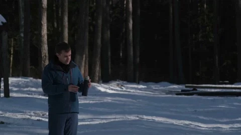 The guy in the forest warms himself with a hot drink from a thermos Vidéo 170481380