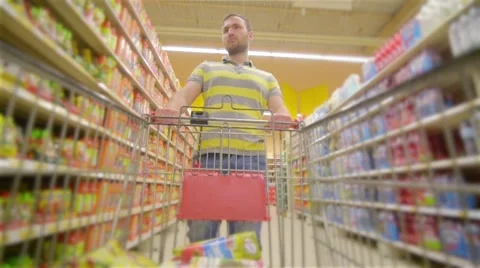 Guy with full supermarket trolley approaching camera, young man chooses products Stock Footage 64744971