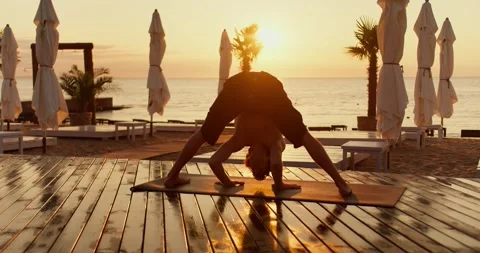 The guy gets on his head in a special yoga exercise on the beach in the morning Stock-Footage 249235259