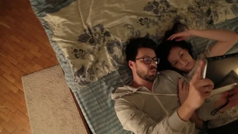 The guy with the girl lying on the bed and watch videos on your tablet with a Fr Stock Footage 73453073