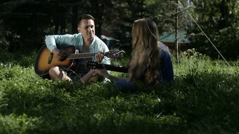 A guy with a girl talking and playing a guitar in the park Stock Footage 80799224