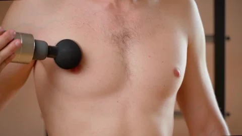 A guy gives himself a self-massage of the pectoral muscle with a percussion Stock Footage 260694625