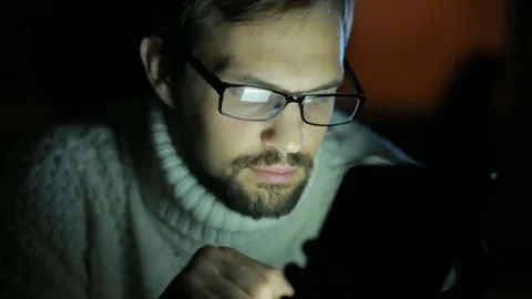 Guy with glasses and a sweater with a tablet in the dark Stock Footage 71188682