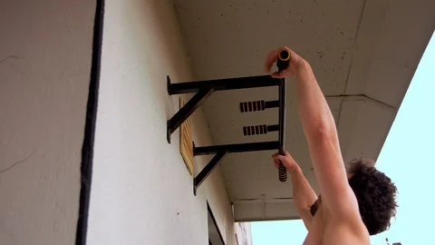 A guy with glasses with a naked torso does pull-ups on the balcony of his Stock Footage 125743721