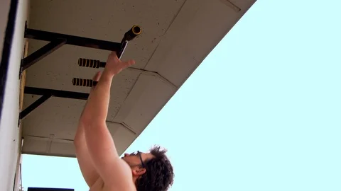 A guy with glasses with a naked torso does reverse pull-ups on the balcony of Stock Footage 125744181