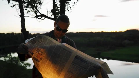 A guy with glasses reads a burning newspaper on the shore at sunset. Stock Footage 138143489