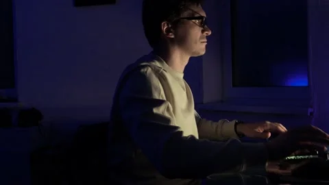 Guy with glasses is sitting in a dark office in front of a monitor Stock Footage 220179492