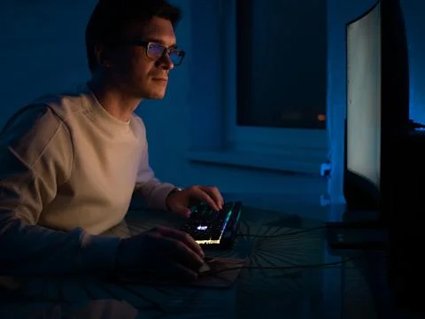 Guy with glasses is sitting in a dark office in front of a monitor Stock Photos