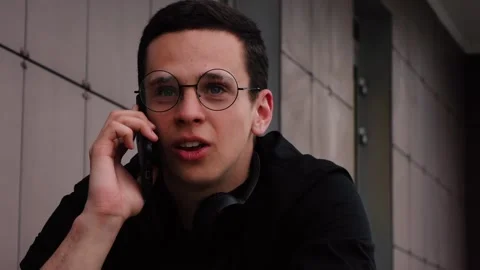 Guy with glasses is talking on the phone while on the street Video stock 133173518