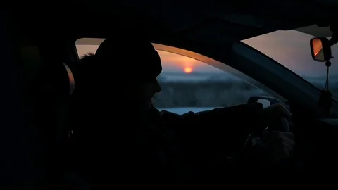 The guy goes behind the wheel of a car. silhouette in winter time at sunset Video stock 69857868