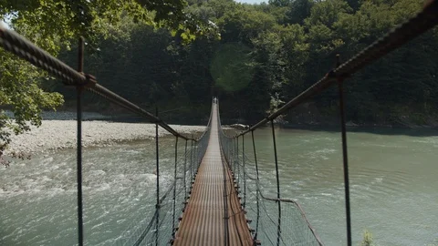 The guy goes on a suspension bridge across the river Stock Footage 112733816