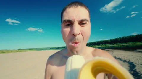 A guy greedily eats a banana on the beach. Video stock 313552466