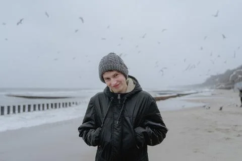 A guy with a grimace on his face in a winter hat and a black jacket stands on Stock Photos