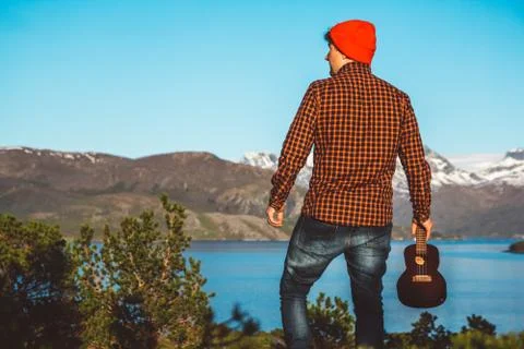 Guy with a guitar on the background of mountains, forests and lakes, wear a s Stock Photos