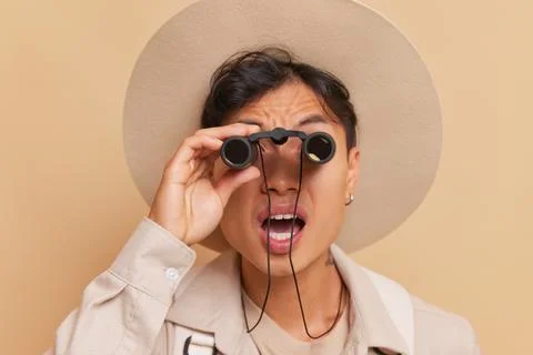 A guy in hat and jacket looks through binoculars with his mouth open in surprise Stock Photos
