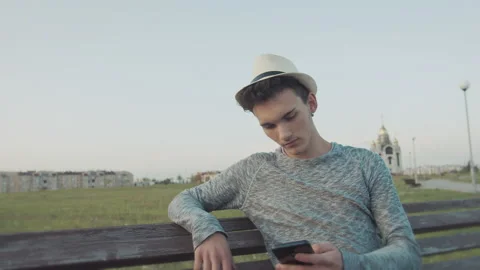 Guy in a hat who sits on an old city bench with a phone, reads messages Stock Footage 164938847
