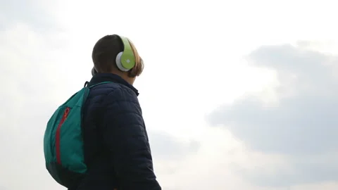The guy in the headphones and with a backpack on the background of a cloudy sky. Stock Footage 105287795