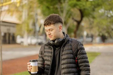 Guy with headphones drinks coffee while walking through a public park. 写真素材