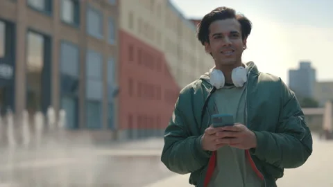 Guy with headphones on neck using mobile while walking Stock Footage 164168607