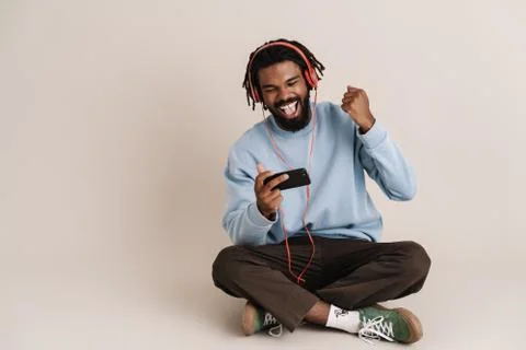 Guy in headphones using cellphone and making winner gesture Stock Photos