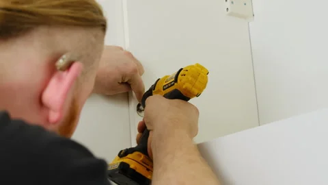Guy with hearing aid works on attaching handle to cabinet door using tool Stock Footage 316188042