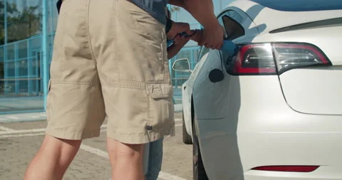 Guy helping a girl to plug in the charging cable in her electric vehicle. Video stock 140054178