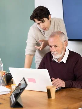 Guy helps elderly man complete task on laptop Stock Photos