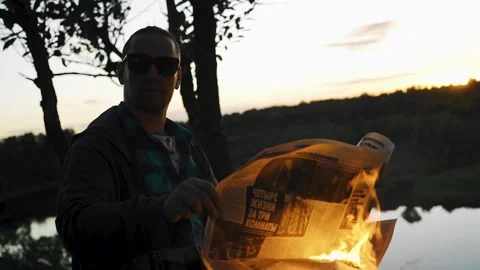 The guy is holding a burning newspaper. The guy is wearing dark glasses. Stock Footage 138143393