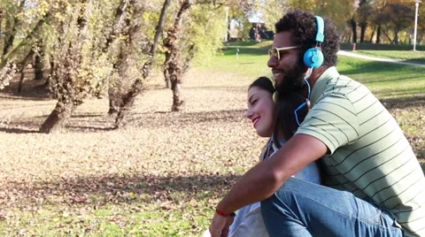 Guy holding girl while they listening to music with headphones at the park Stock Footage 59555643