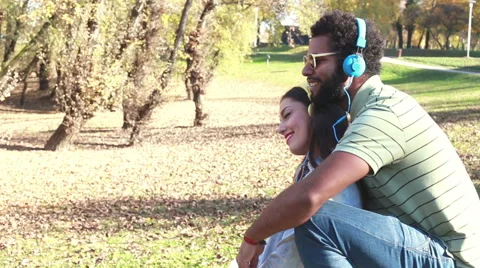 Guy holding girl while they listening to music with headphones at the park Stock Footage 59555647