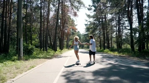 Guy holds girl's hand when she rides a skateboard Stock Footage 99678260