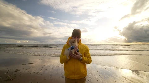 The guy holds in his hands a small dog in autumn on the seashore Stock Footage 172055654