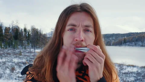 Guy holds his lips, makes sounds with fingers on jews harp Video stock 257060118
