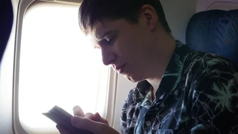 The guy holds the mobile phone in the plane near the window 库存影片 74703090