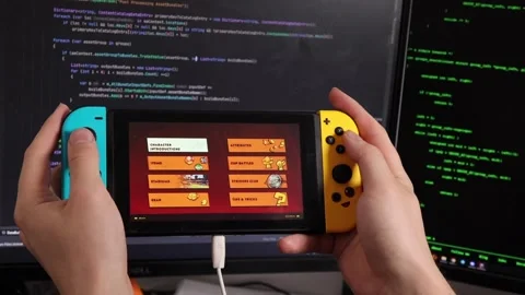 A guy holds a Nintendo switch in his hands against the background of a monitor Stock Footage 219565094
