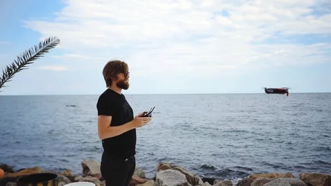 Guy holds remote control drone flies over sea slow motion Stock Footage 113788148