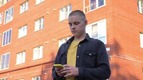 Guy holds a yellow smartphone, standing against the background of a red brick Stock Footage 283438368