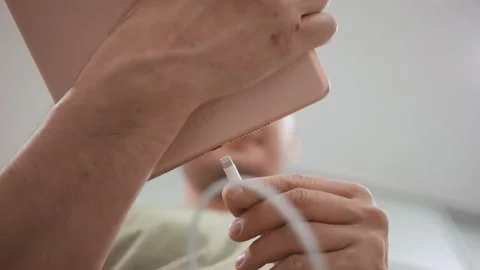 The guy inserts the cable to charge the tablet. Bottom view. Stockbeeldmateriaal 150331940