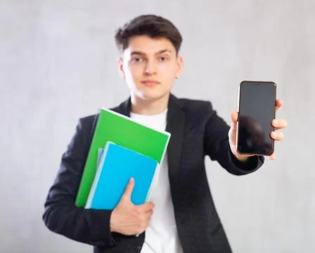 Guy in jacket with stack of notebooks shows empty mobile phone screen.Device Foto stock
