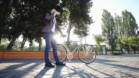 Guy in a jacket stands with a bicycle and drinks coffee in the rays of dawn Stock Footage 121131107