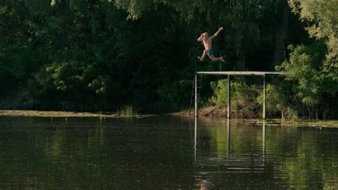 A guy jumps into the lake from the jetty at sunset Video stock 203903671