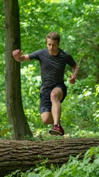 The guy jumps over a large log while participating in an ocr race Stock Photos