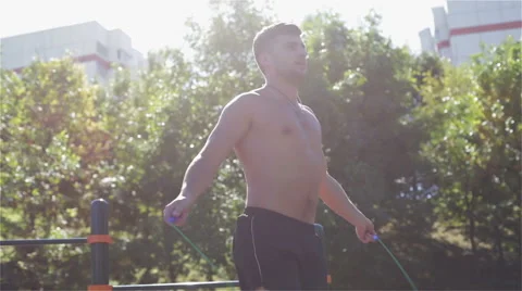 The guy jumps on a skipping rope outdoors in a bright sunlight. Stock Footage 68064488