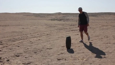 A guy kicks a tire from a wheel in the desert Stock Footage 82453462