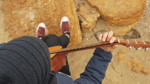 The guy in the knitted hat sits on a stone and plays the guitar.playing guita Stock Footage 103445324