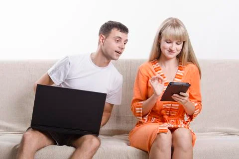 Guy with laptop sitting on couch, looking at tablet girl Foto stock