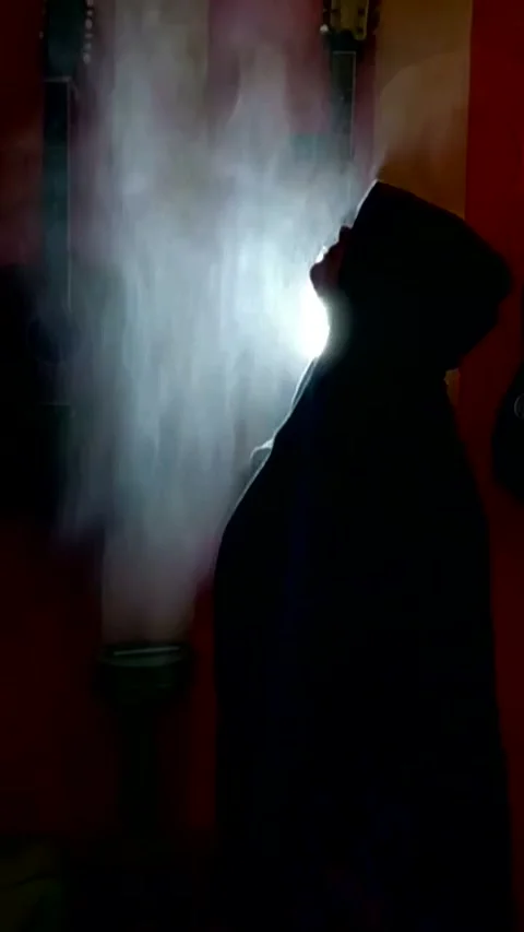 A guy in a large, deep black hoodie raises his head Stock Footage 328371484