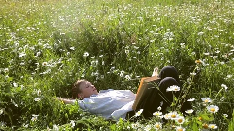 Guy laying on the grass and reading a book 스톡 동영상 78255038