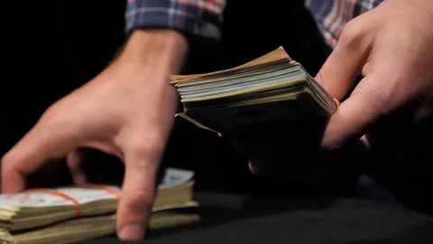 The guy lays a stack of dollars on the background of a bundle of money. Video stock 129786347